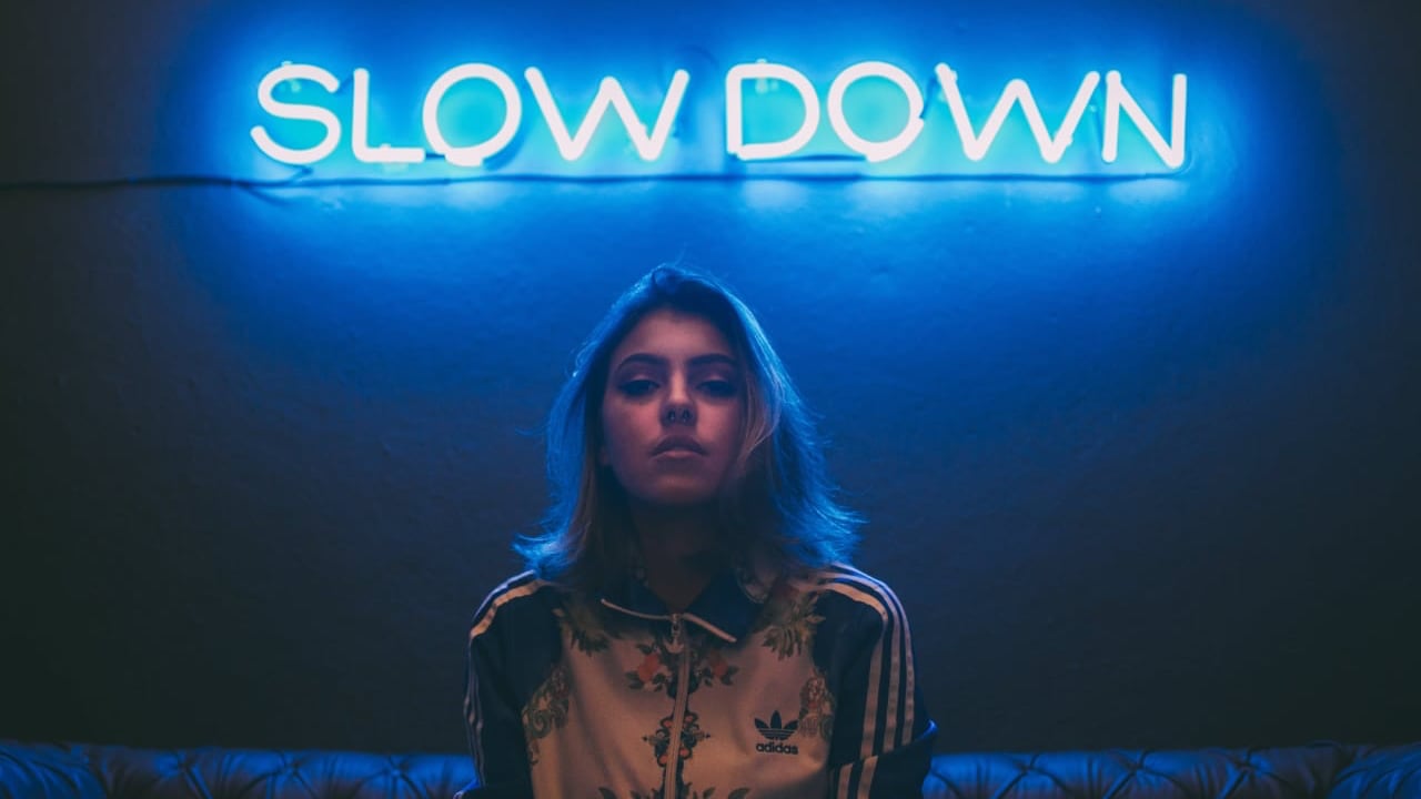 Photo of a woman standing in front of a neon sign that says 'Slow Down'