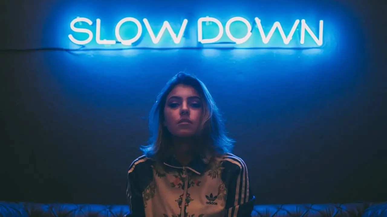 Photo of a woman standing in front of a neon sign that says 'Slow Down'